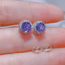 Purple gemstone earrings on a hand with a blurred background