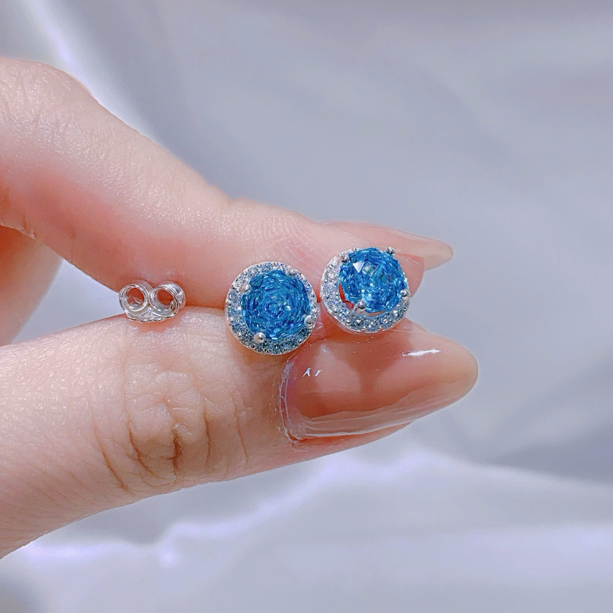 Blue gemstone earrings held between fingers against a neutral background