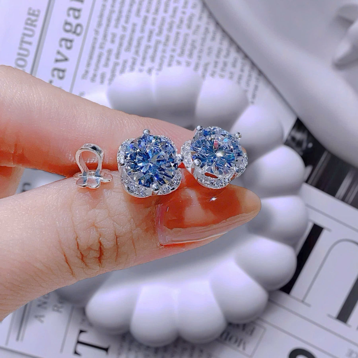 Blue gemstone earrings held between fingers on a newspaper background