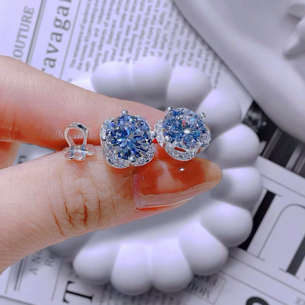 Blue gemstone earrings held between fingers on a newspaper background