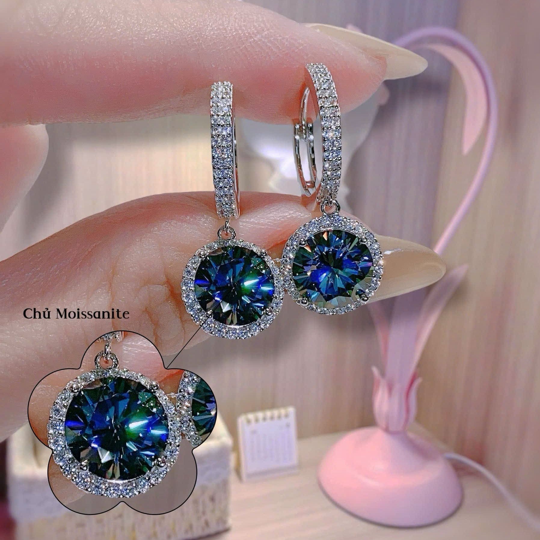 Blue gemstone earrings held by a hand with a blurred background
