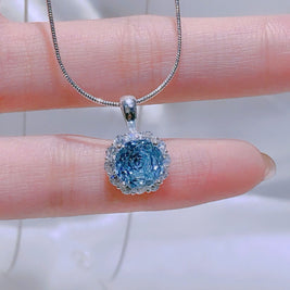 Blue gemstone pendant on a chain held between fingers against a blurred background