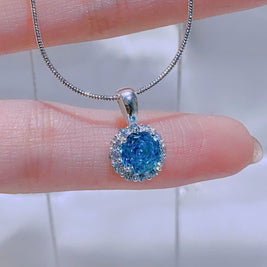 Blue gemstone pendant on a silver chain held by a hand against a neutral background