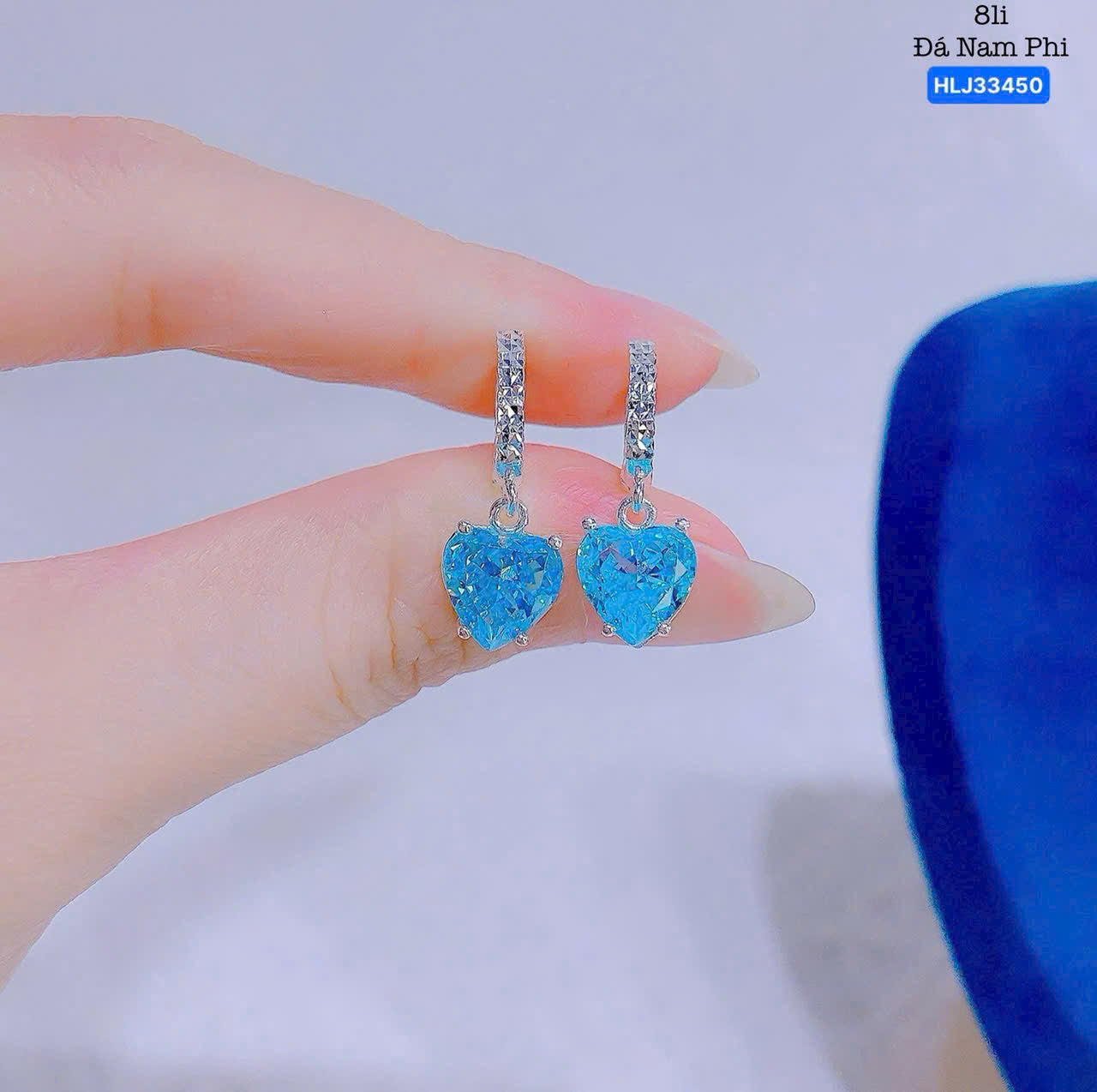 Blue heart-shaped earrings held between fingers against a neutral background