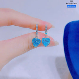 Blue heart-shaped earrings held between fingers against a neutral background