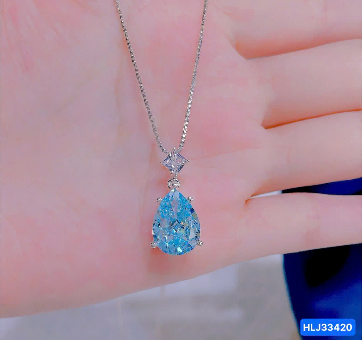 Blue teardrop pendant on a chain held against a hand