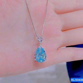 Blue teardrop pendant on a chain held against a hand