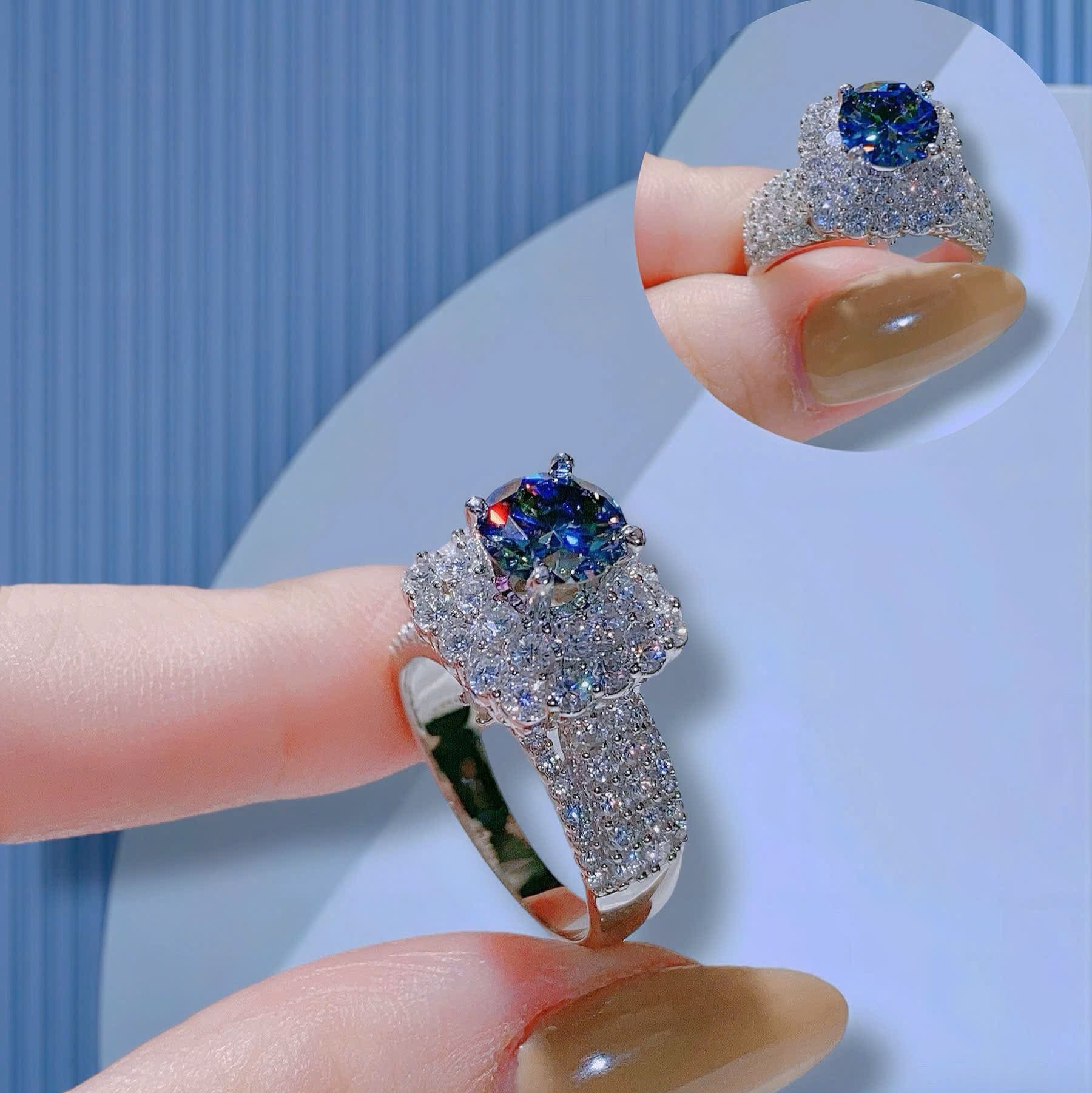 Close-up of a hand holding a silver ring with a blue gemstone against a light blue background.