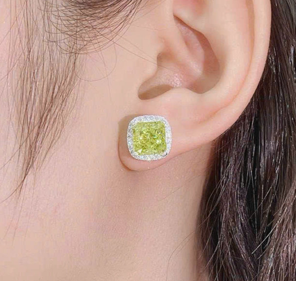 Close-up of an ear wearing a green gemstone earring with a plain background