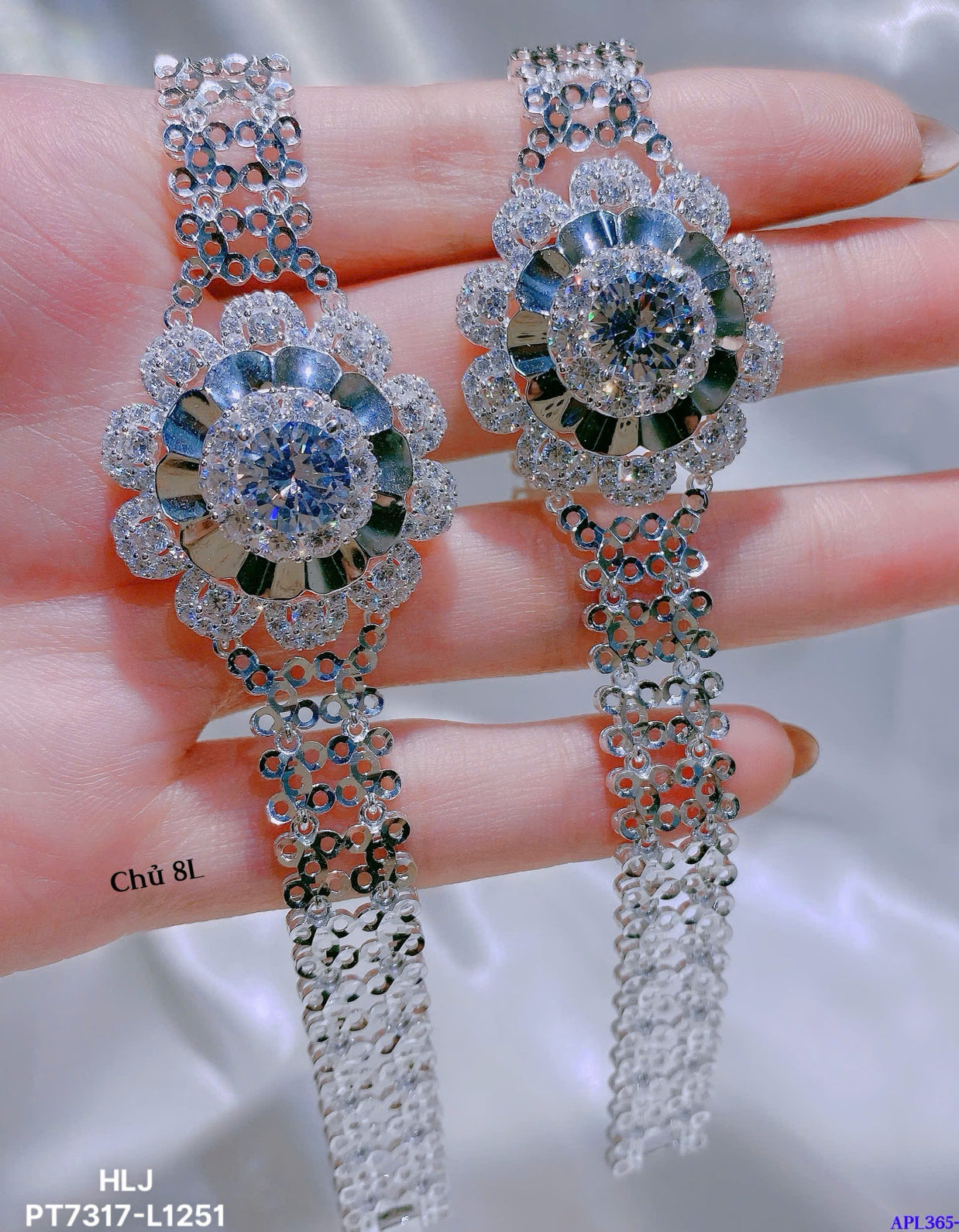 Delicate silver earrings with gemstones held between fingers against a neutral background