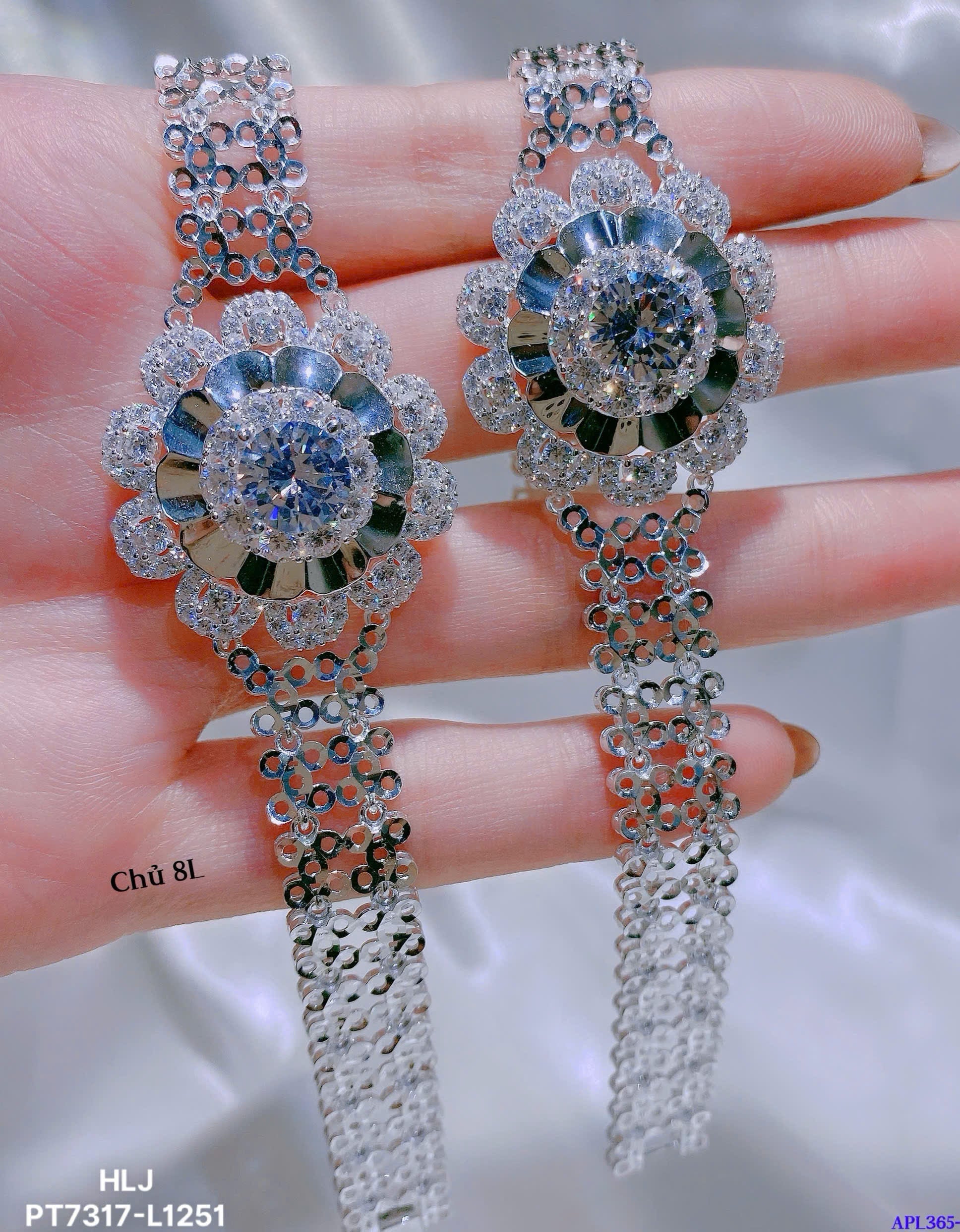Delicate silver earrings with gemstones held between fingers against a neutral background