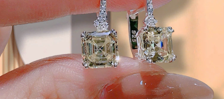 Diamond earrings held between fingers with a blurred background