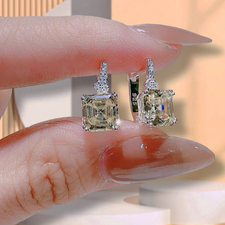 Diamond earrings held between fingers with a blurred background