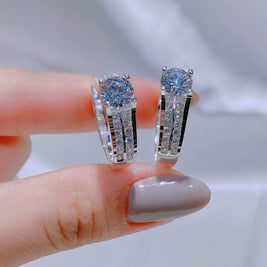 Diamond earrings held between fingers against a neutral background