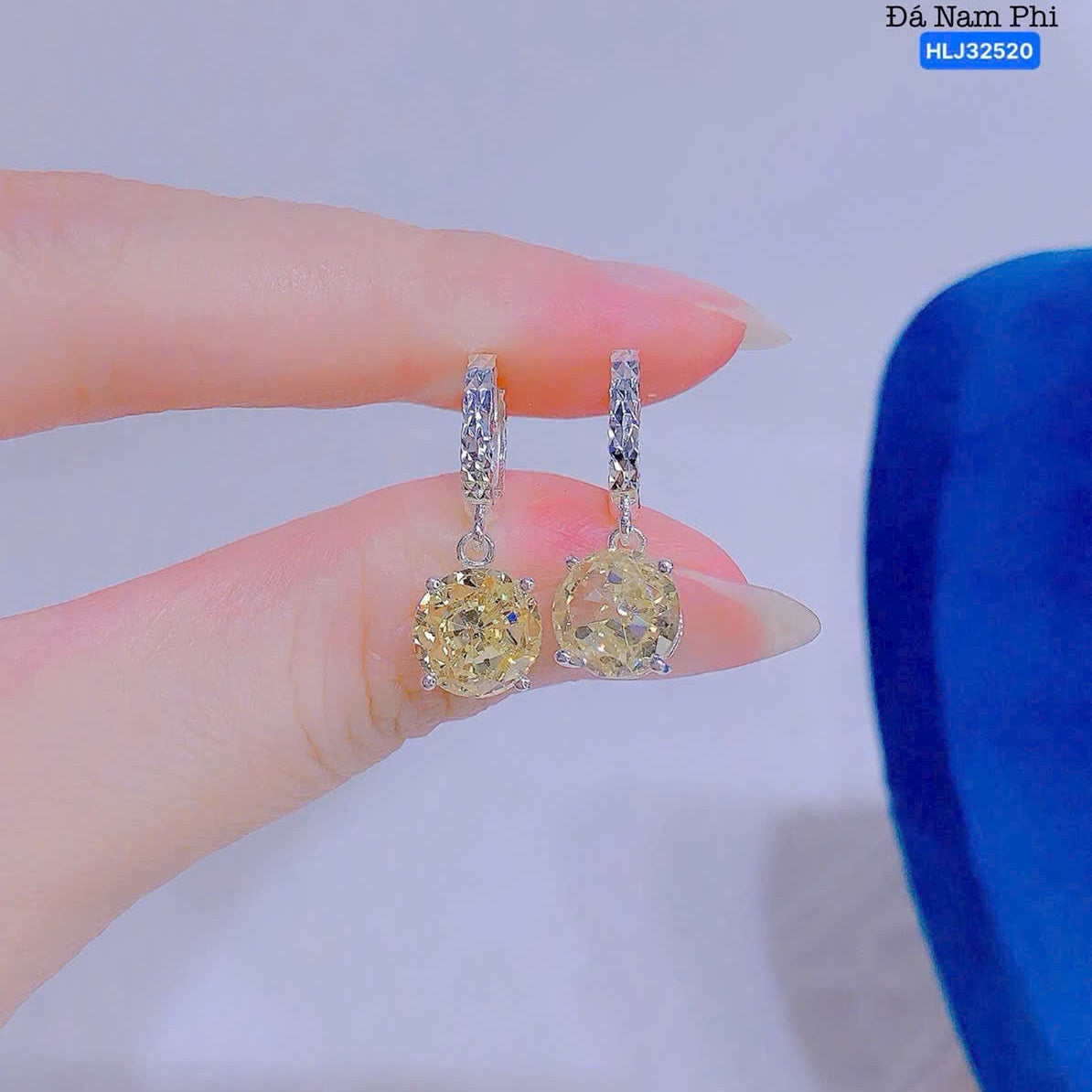 Diamond earrings held between fingers with a blue jewelry box in the background