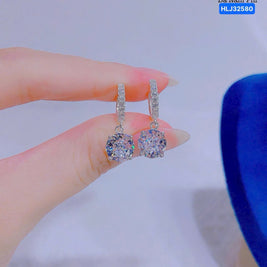 Diamond earrings held between fingers with a blurred background