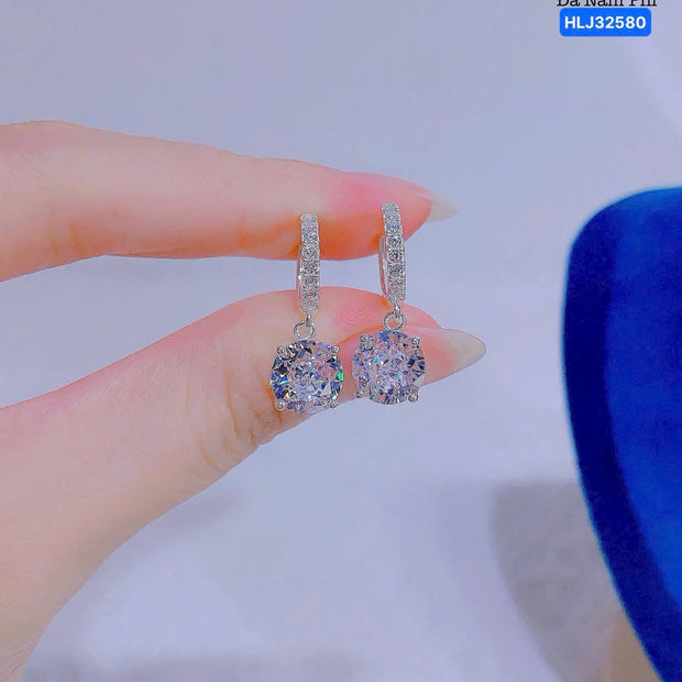Diamond earrings held between fingers with a blurred background
