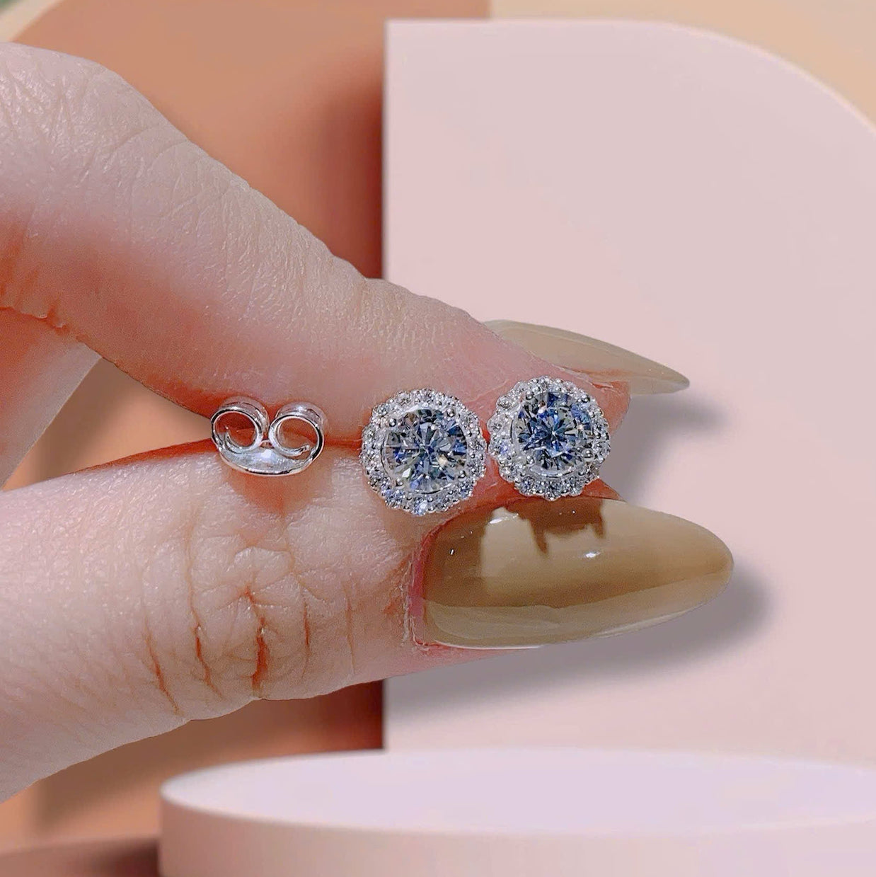 Diamond earrings held between fingers with a neutral background