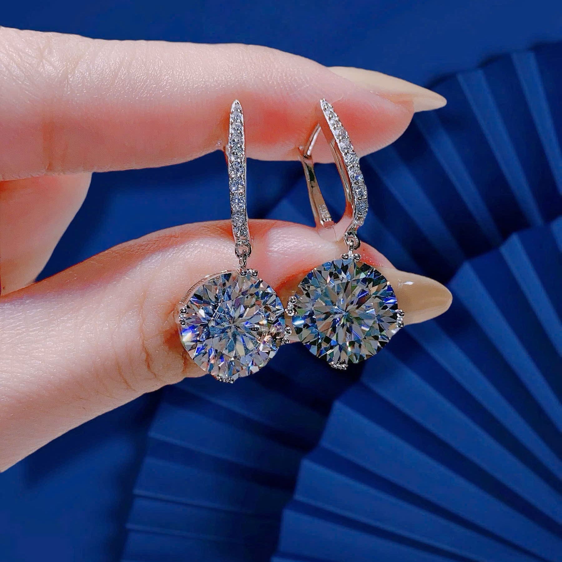 Diamond earrings held by a hand against a blue background
