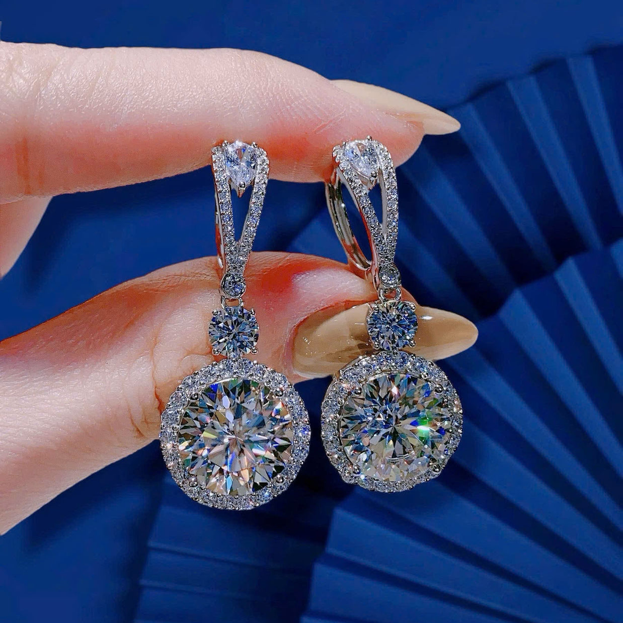Diamond earrings held by a hand against a blue background