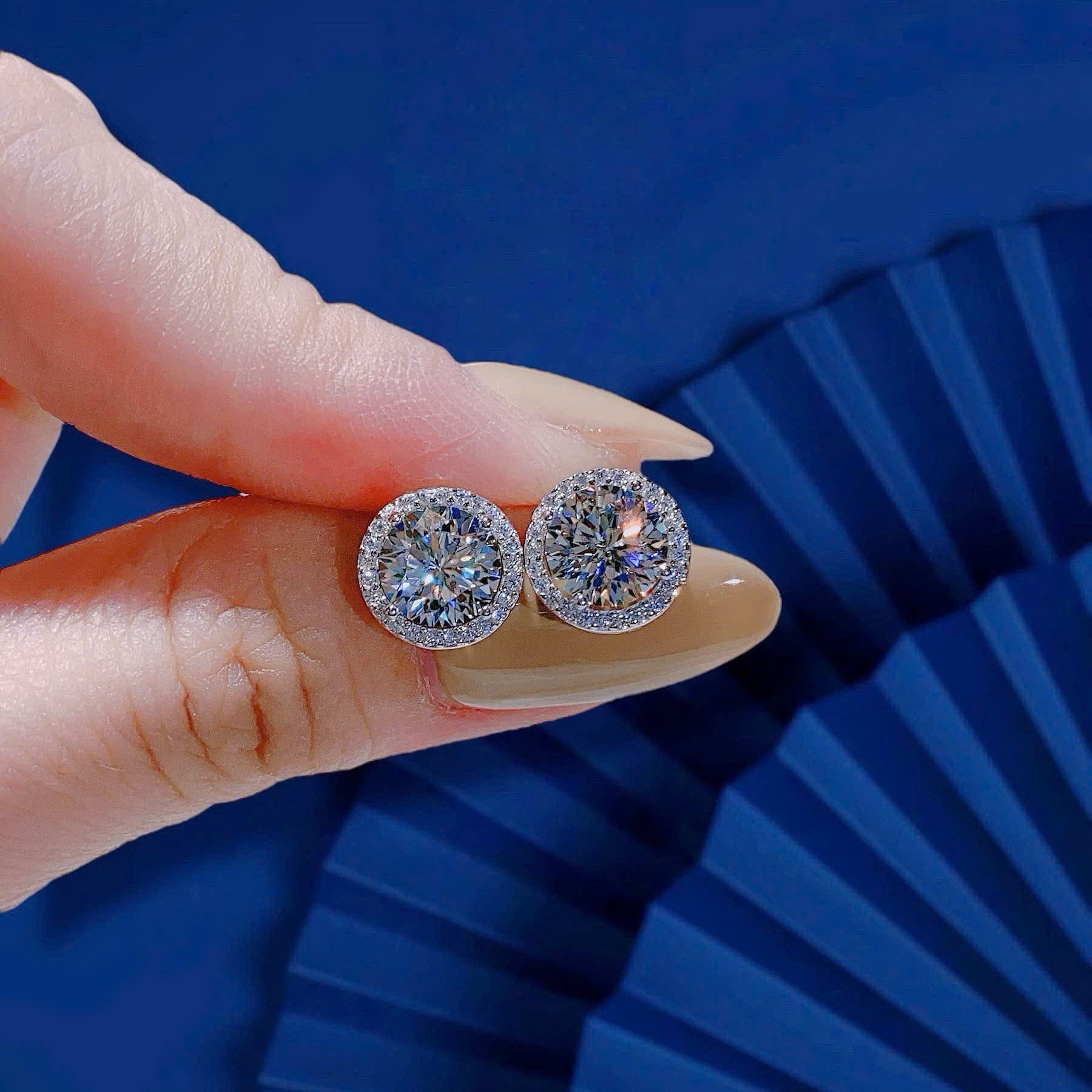 Diamond earrings held by a hand against a blue background
