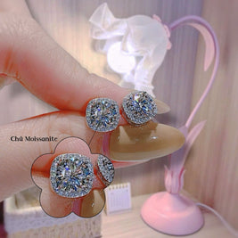 Diamond earrings held by a hand with a blurred background