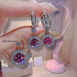 Diamond earrings with red gemstones held by a hand against a blurred background
