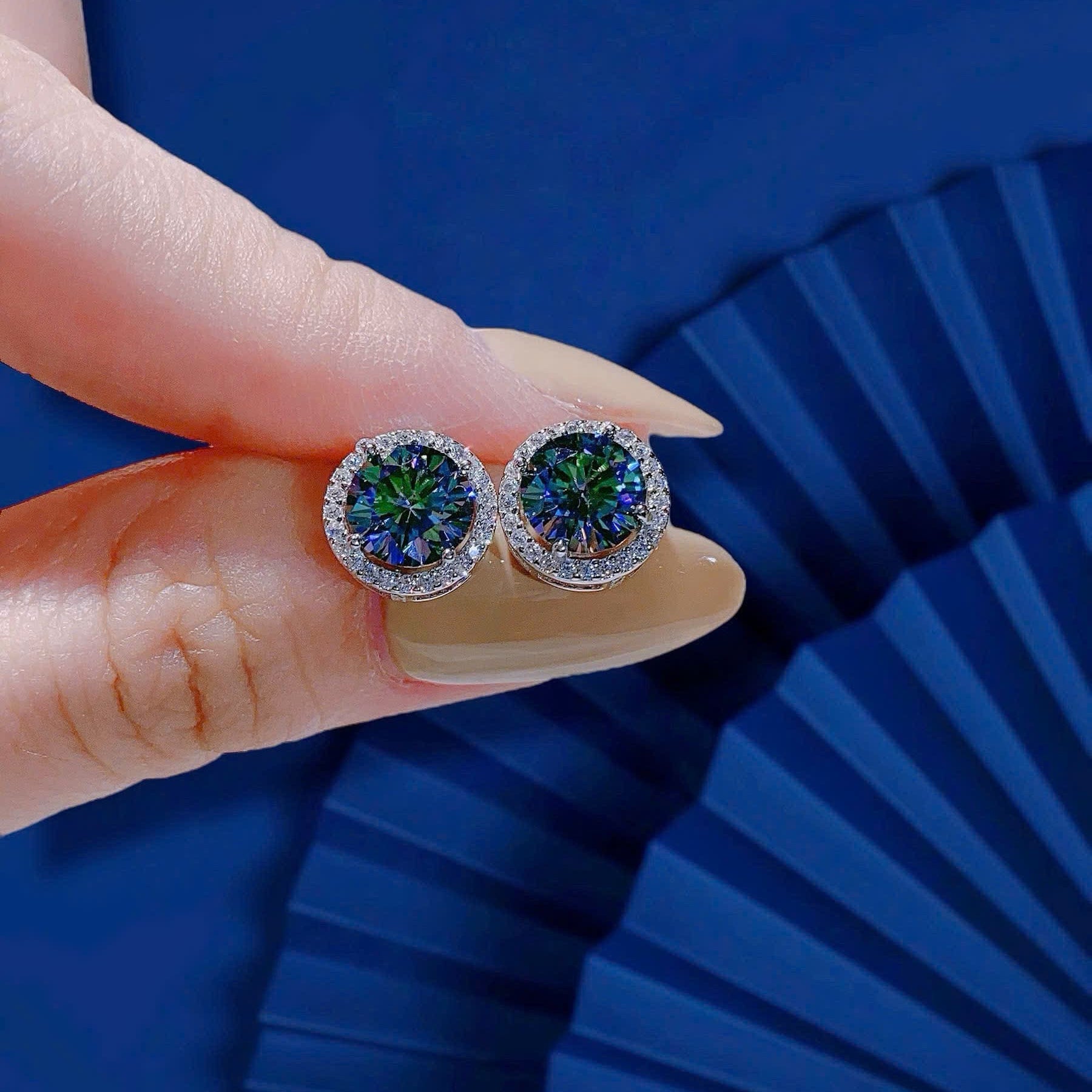 Earrings held between fingers against a blue background
