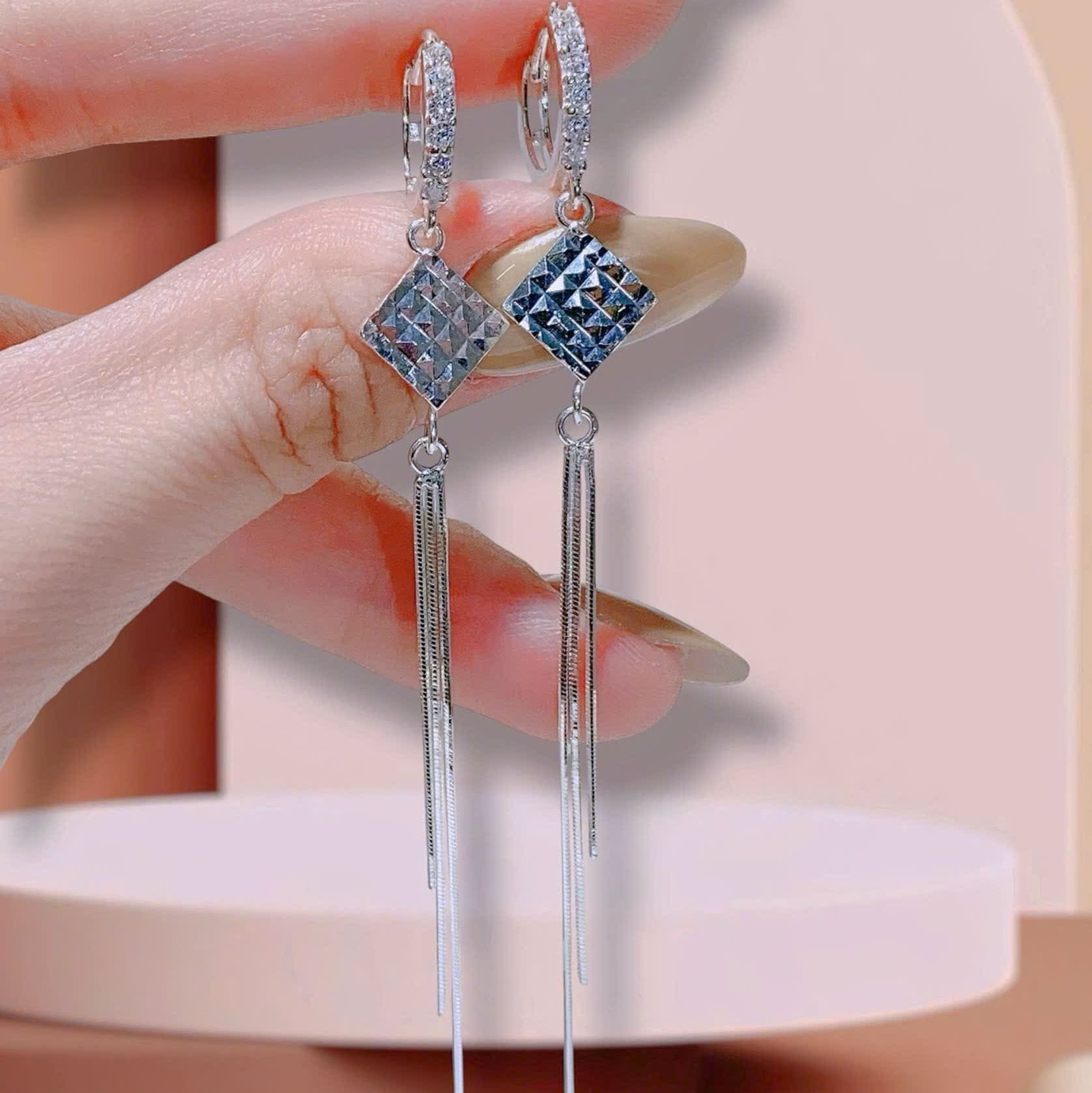 Earrings with blue gemstones held by a hand against a neutral background