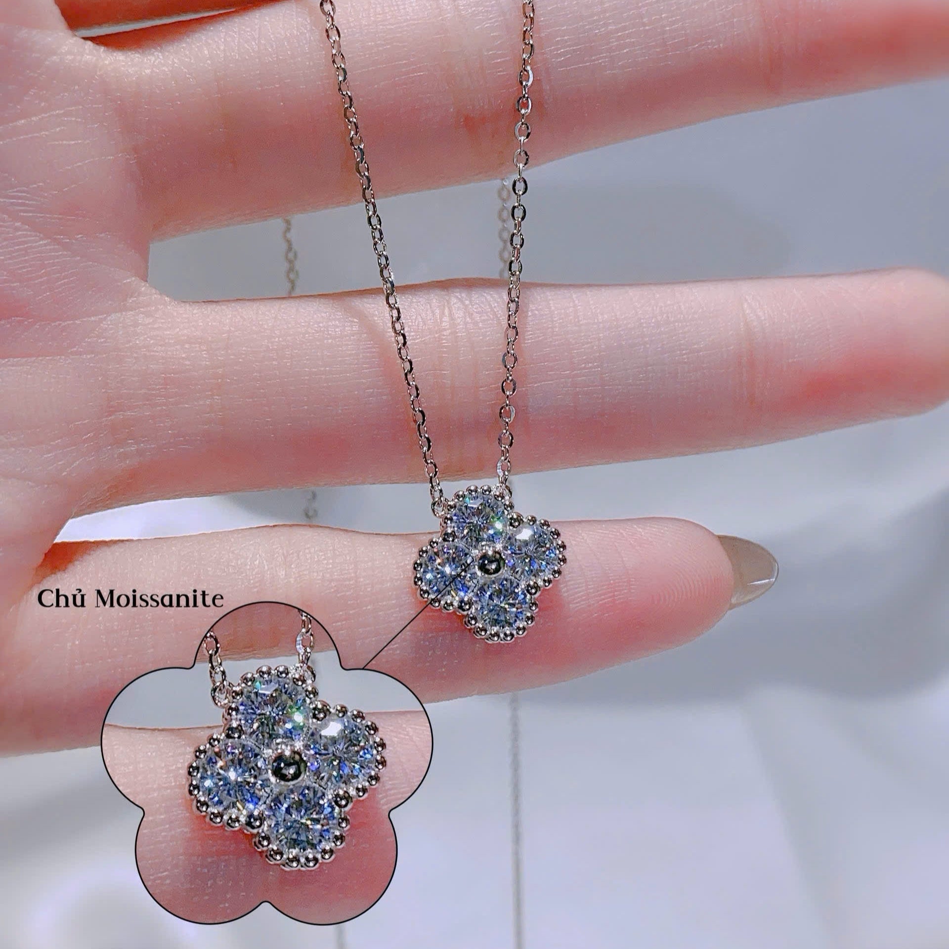 Flower-shaped jewelry with Moissanite stones on a hand, with close-up inset showing details.