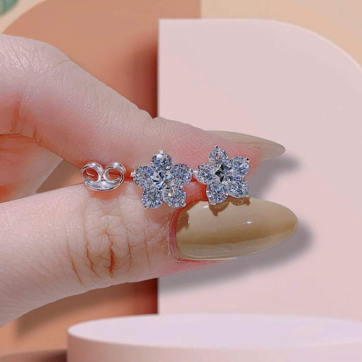 Flower-shaped silver earrings on a finger with a pink background