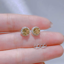 Gold earrings held between fingers with a blurred background