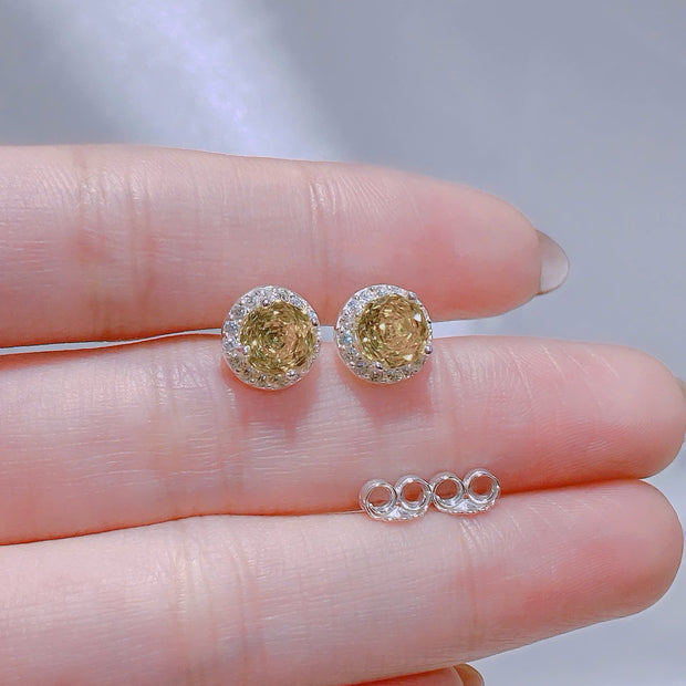 Gold earrings held between fingers with a blurred background