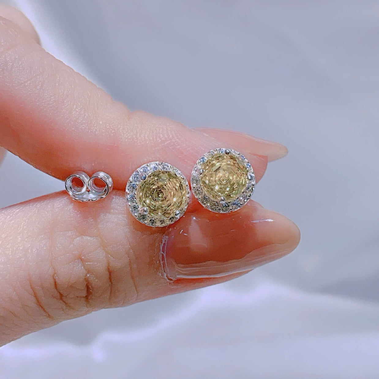 Gold earrings with gemstones held between fingers against a neutral background