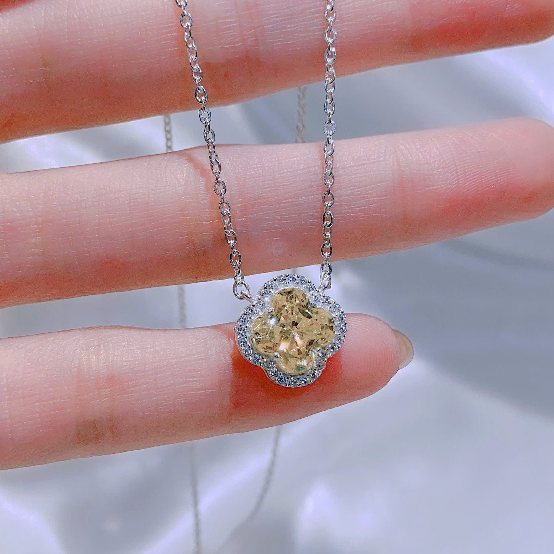 Gold heart-shaped pendant on a silver chain held by a hand against a blurred background