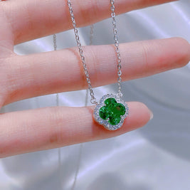 Green clover-shaped pendant on a silver chain held between fingers against a blurred background