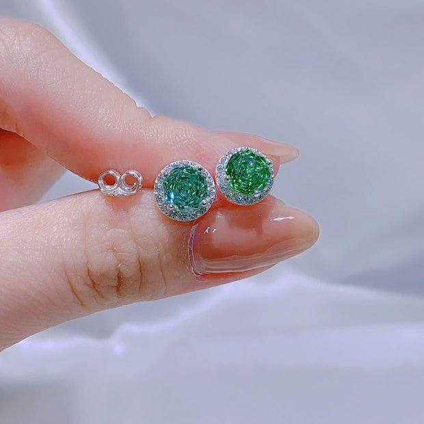 Green gemstone earrings held between fingers against a neutral background