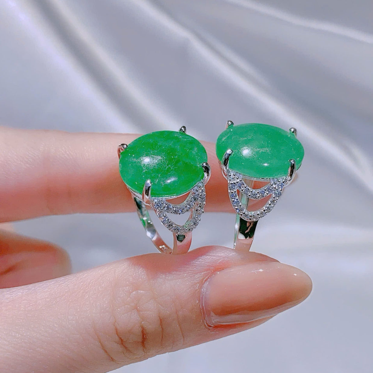 Green gemstone earrings held between fingers against a neutral background