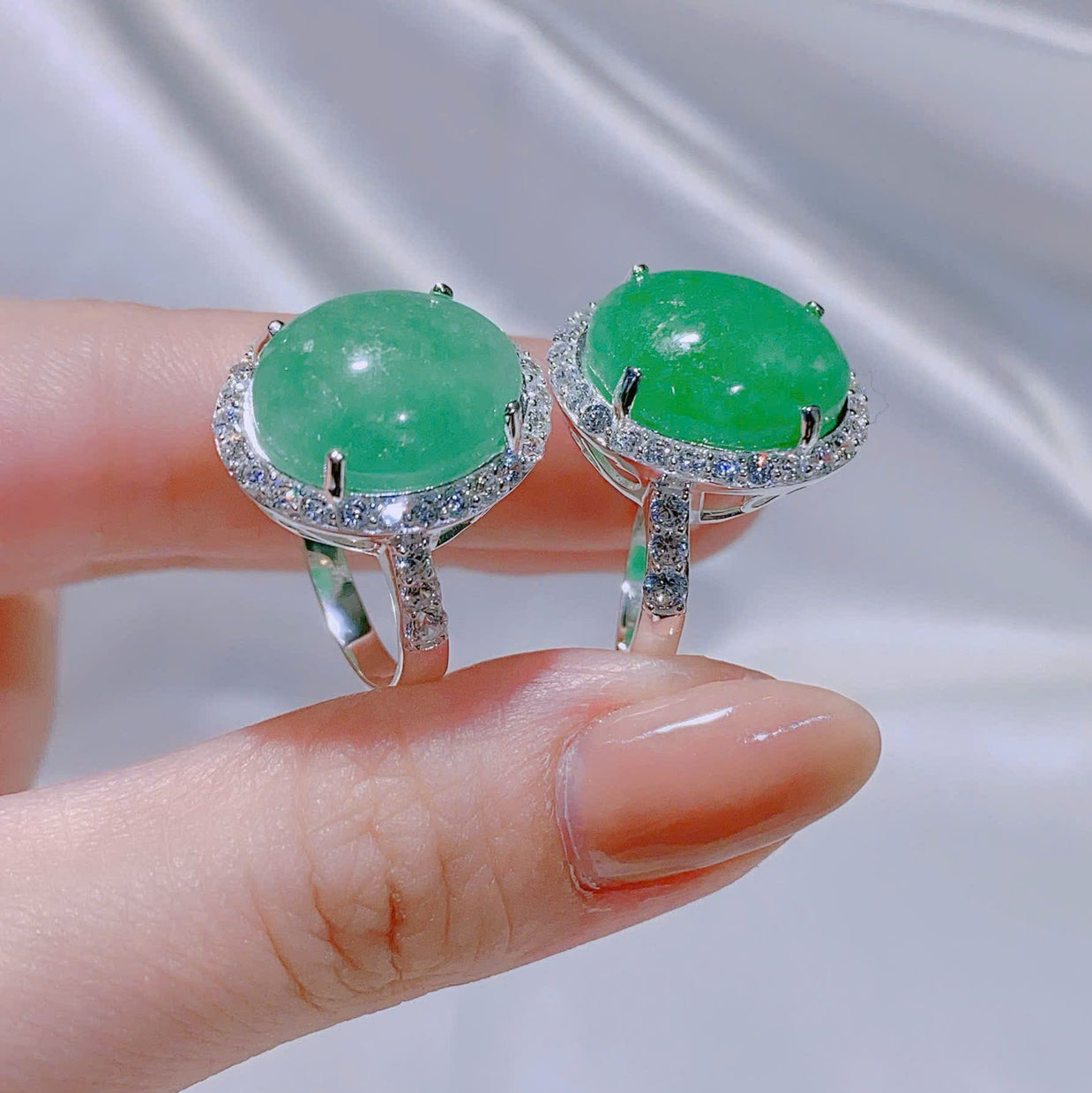 Green gemstone earrings held between fingers against a neutral background