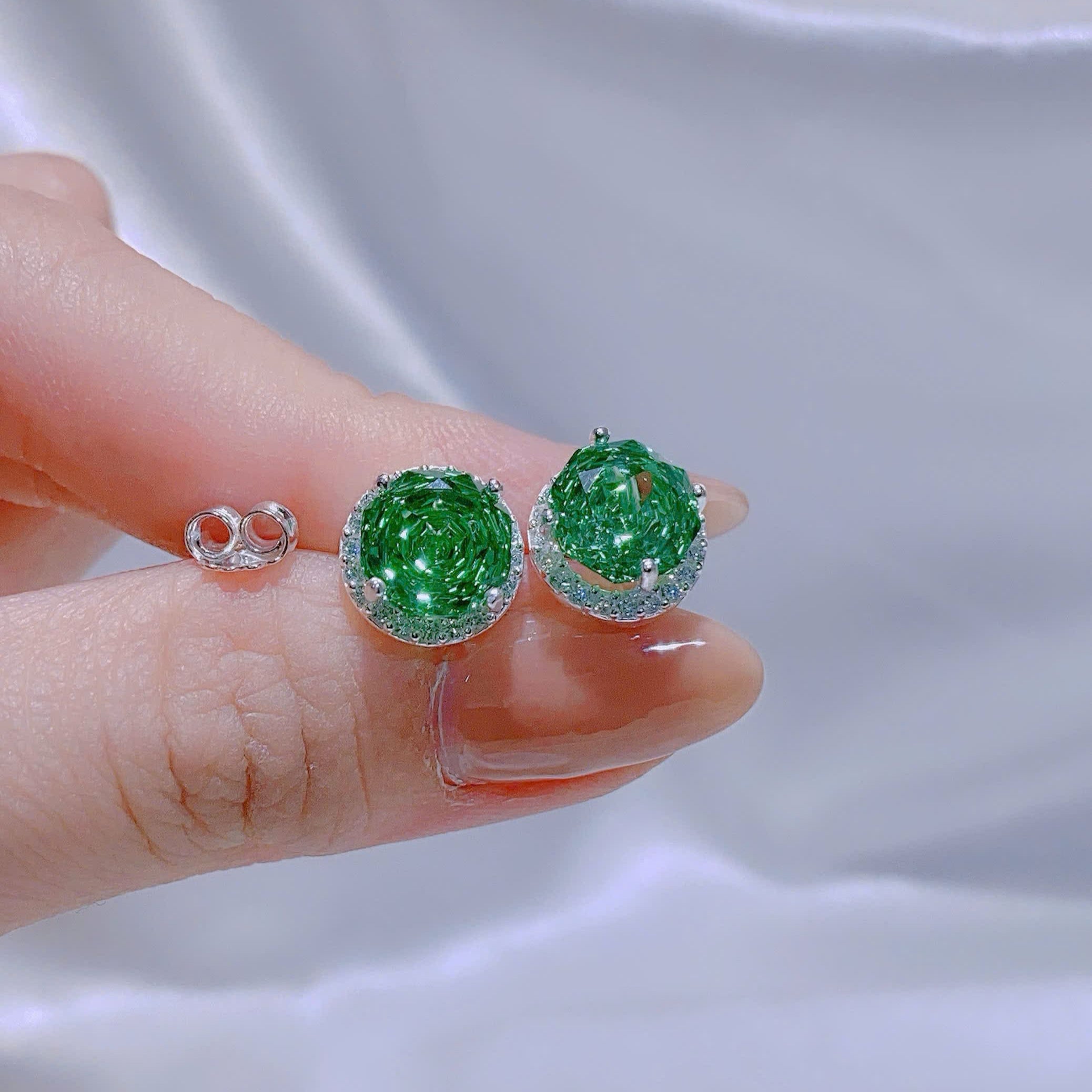 Green gemstone earrings held between fingers against a white background