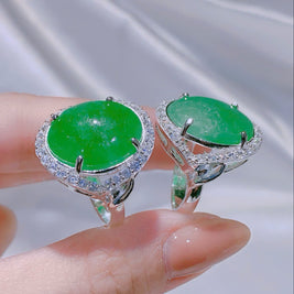 Green gemstone earrings held on a hand with a blurred background