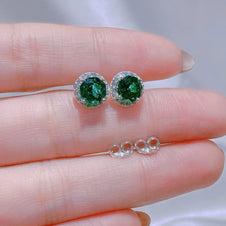 Green gemstone earrings on a hand with a blurred background