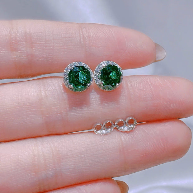 Green gemstone earrings on a hand with a blurred background