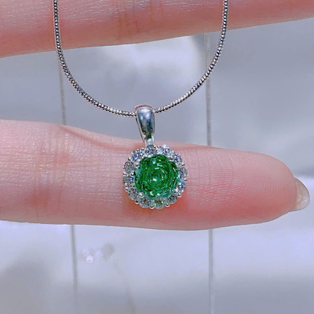 Green gemstone pendant on a silver chain held between fingers