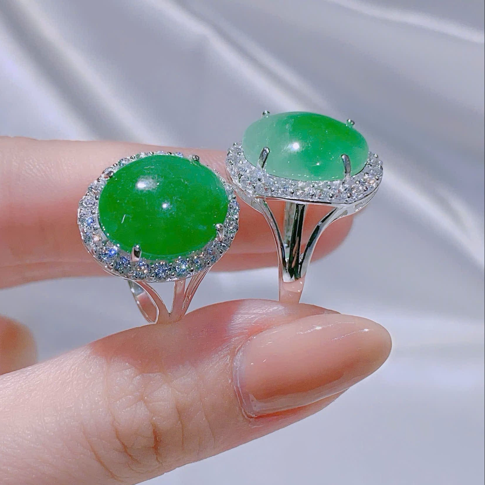 Green gemstone ring with silver band held by a hand against a neutral background