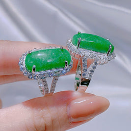 Green gemstone ring with silver band held by a hand against a neutral background