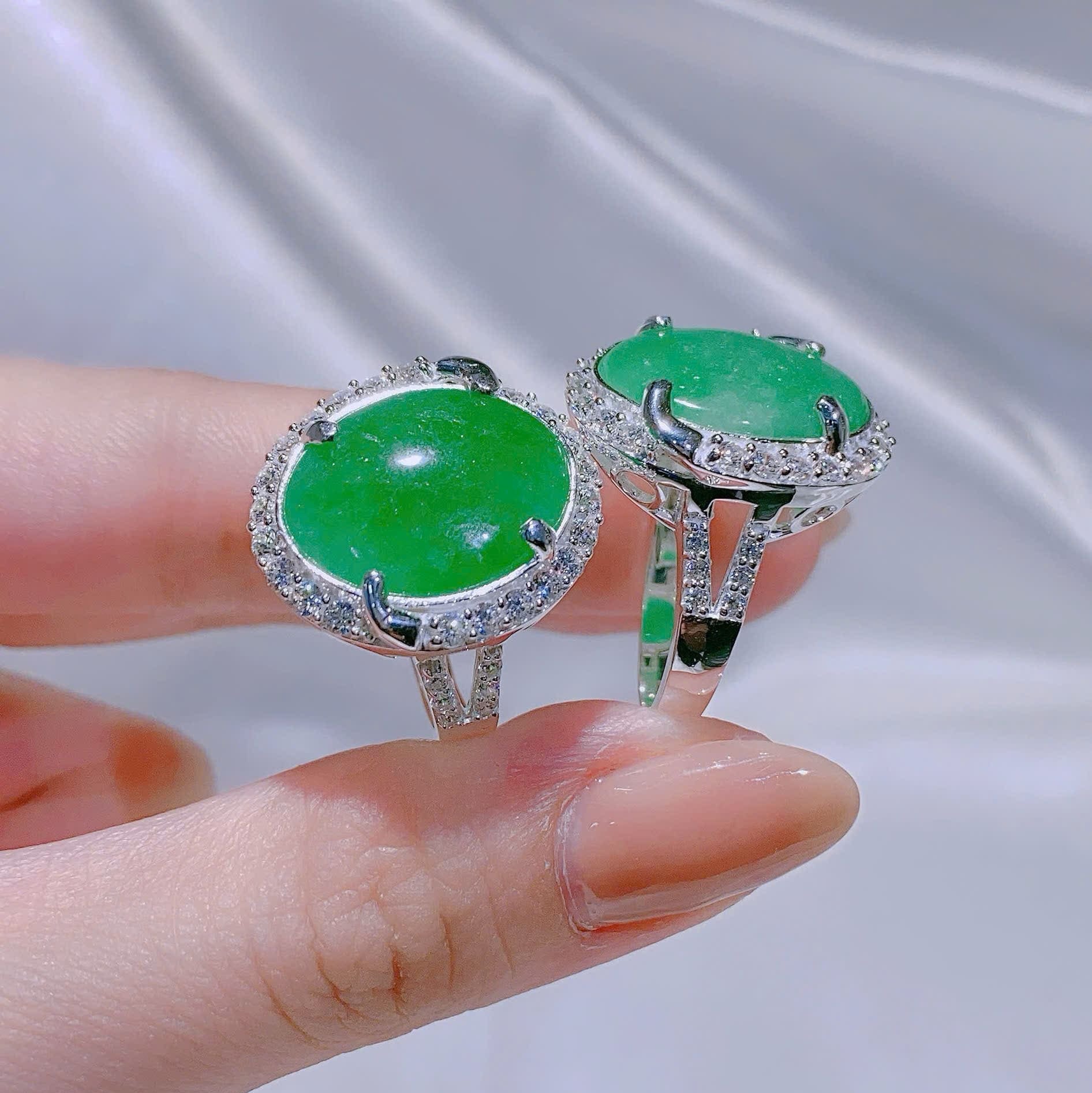 Green gemstone rings held between fingers against a neutral background