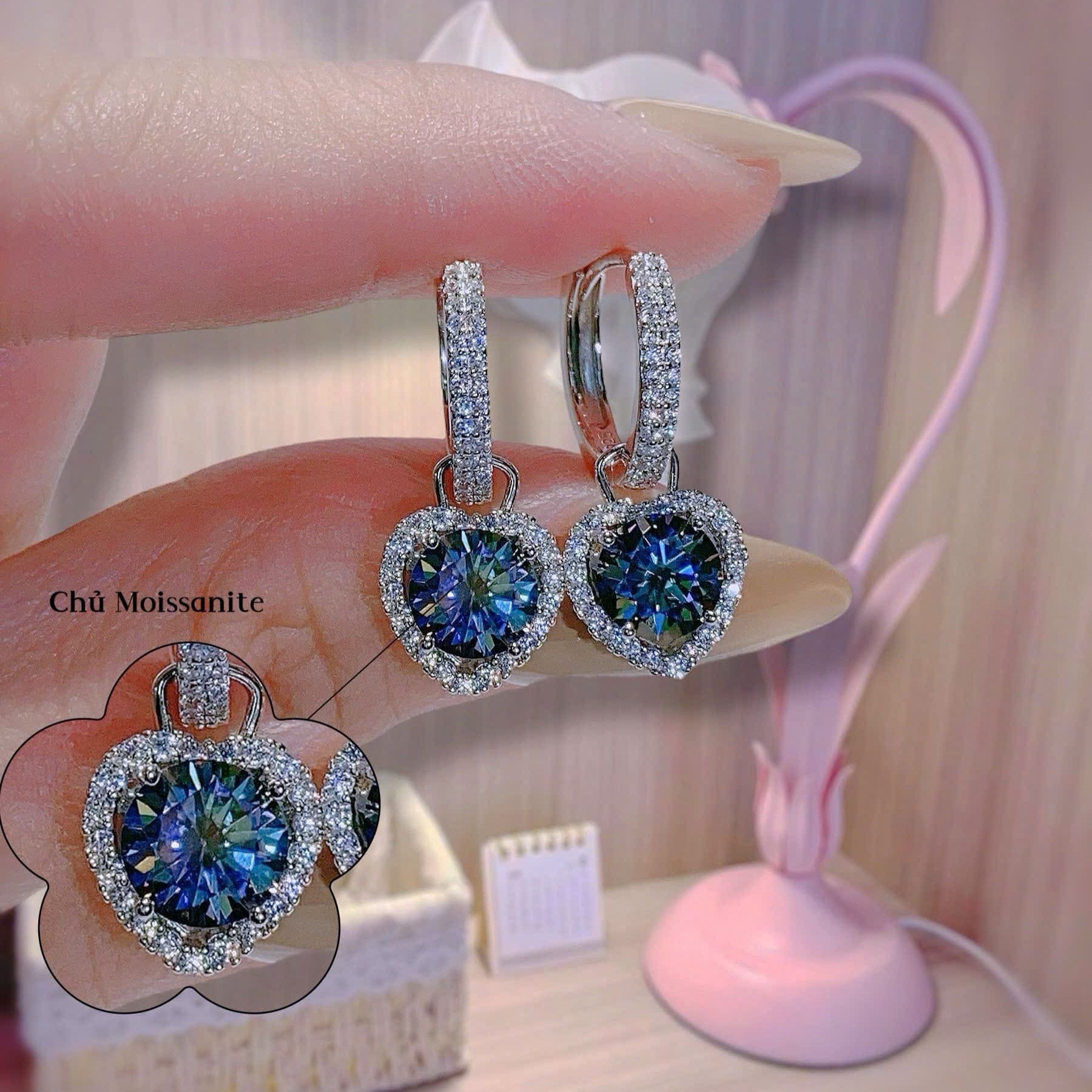 Heart-shaped blue gemstone earrings with diamond accents held by a hand.