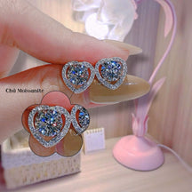 Heart-shaped diamond earrings held by a hand with a blurred background