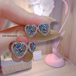 Heart-shaped diamond earrings held by a hand with a blurred background